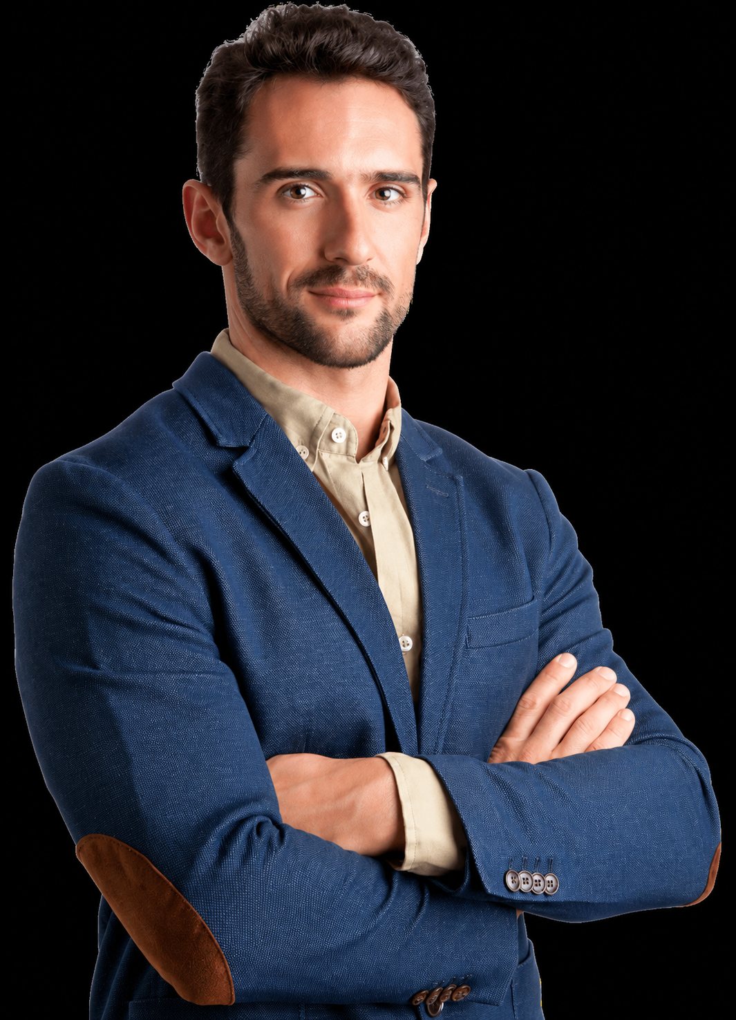 Un homme brun avec une barbe courte pose les bras croisés, vêtu d’une veste bleue à coudières marron et d’une chemise beige.